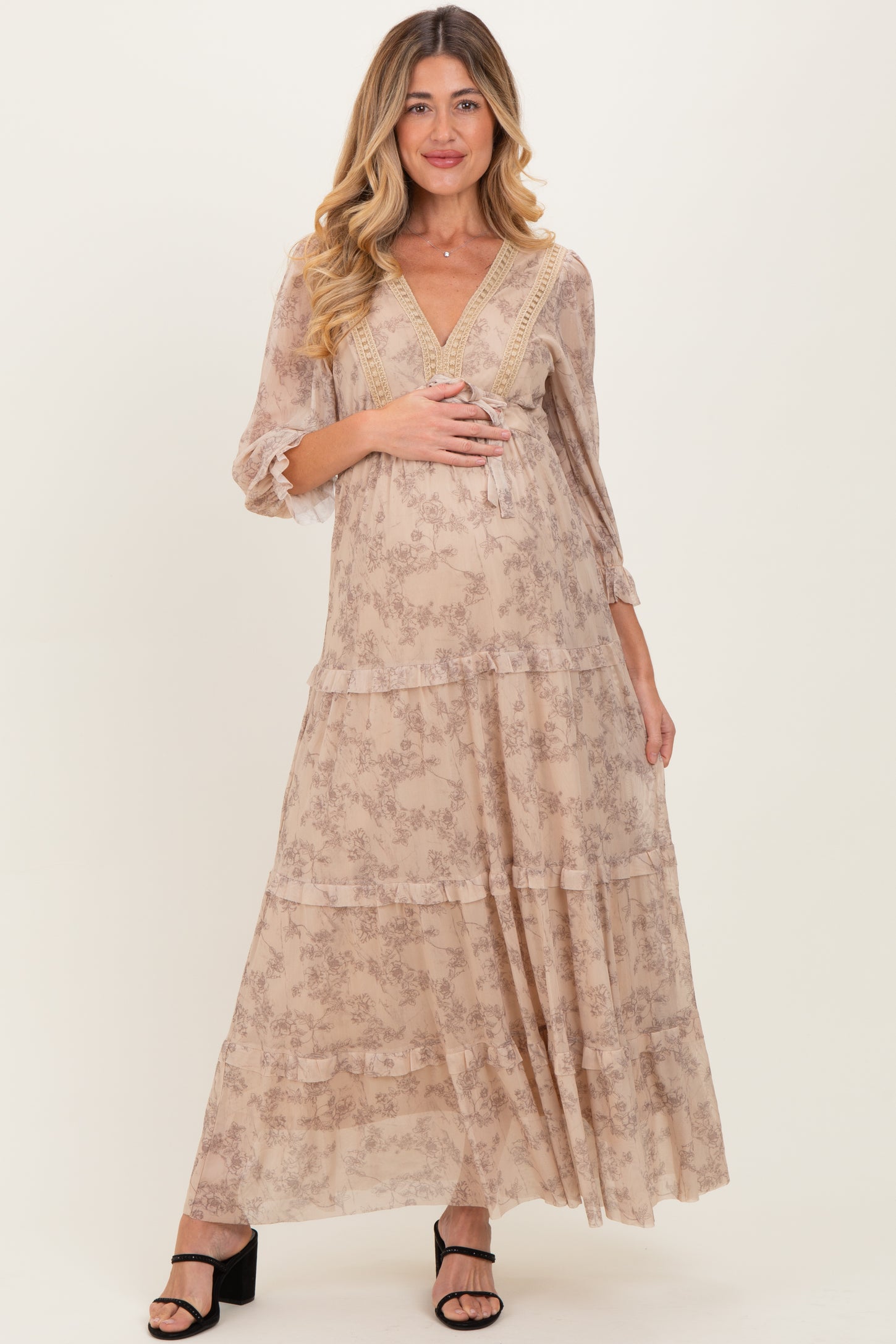 woman wearing a flowy beige floral maternity maxi dress with three-quarter sleeves and a visible baby bump