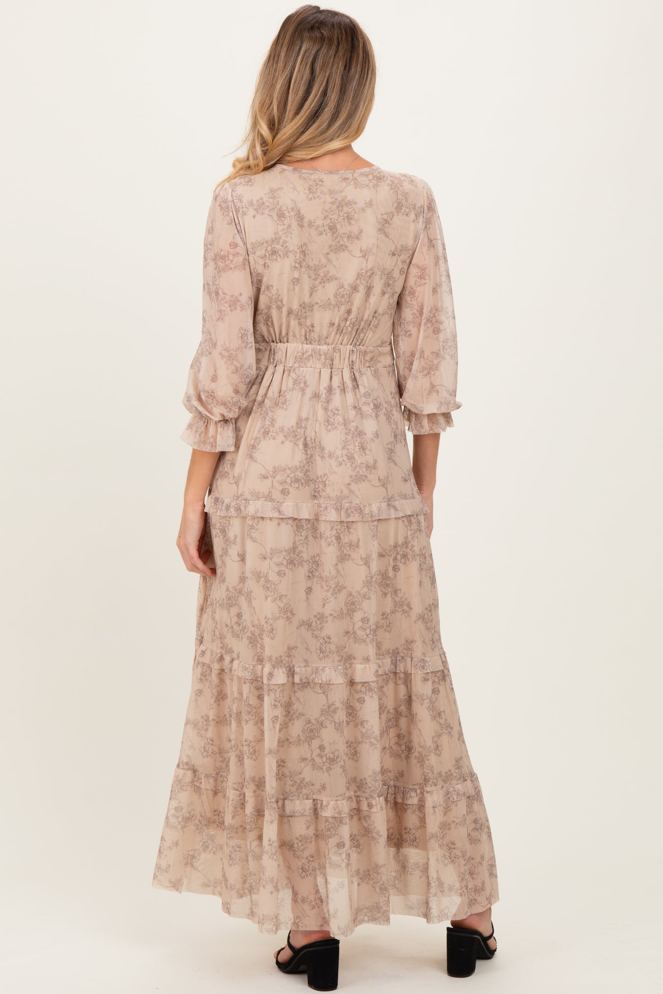 woman wearing a beige floral maternity maxi dress with ruffle sleeve details, showcasing a flowing silhouette from the back