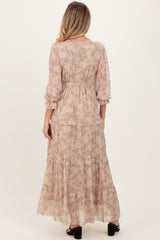 woman wearing a beige floral maternity maxi dress with ruffle sleeve details, showcasing a flowing silhouette from the back