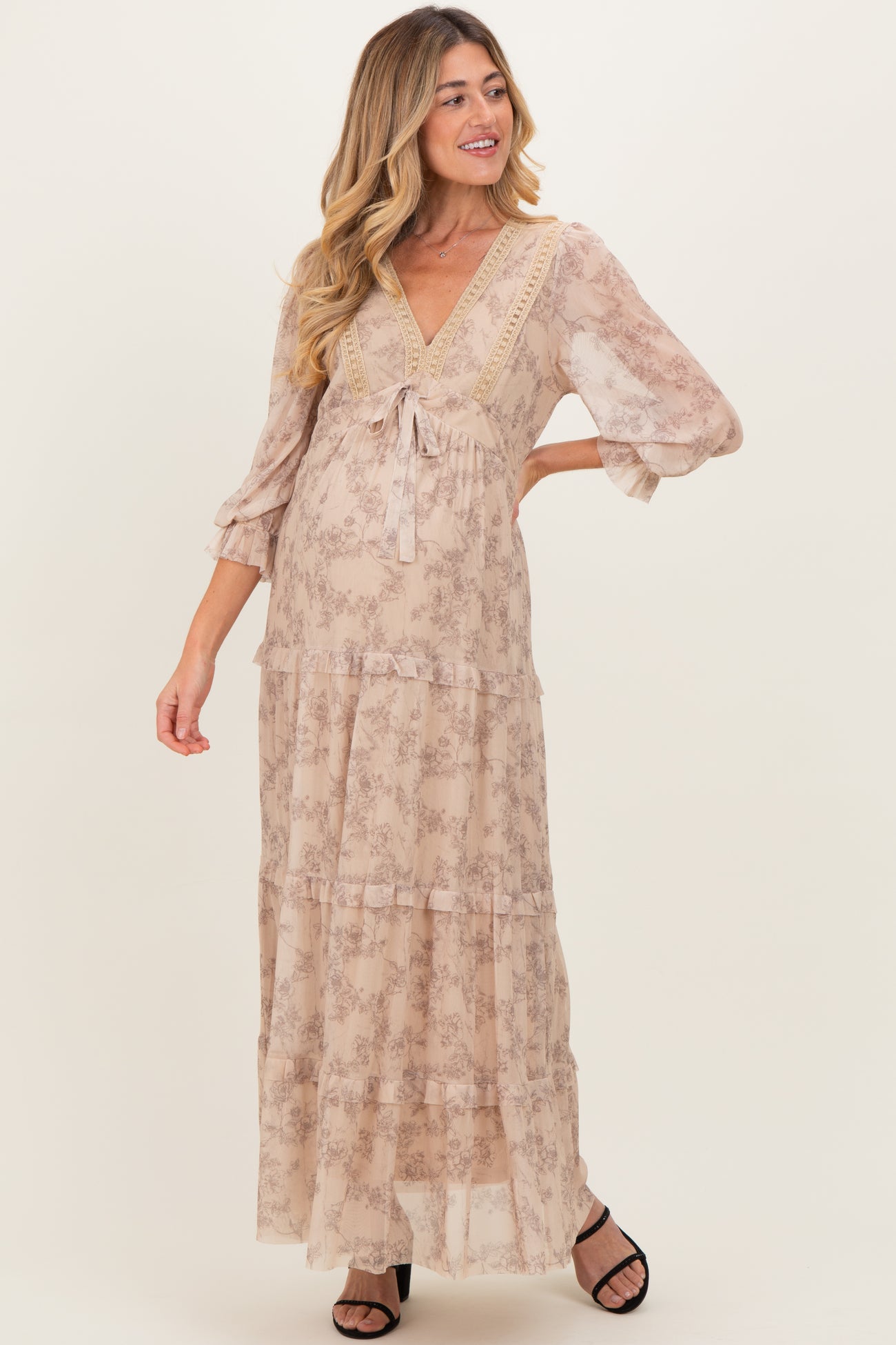 woman wearing a light floral print maternity maxi dress with a v-neckline and tiered ruffles, showing off her baby bump