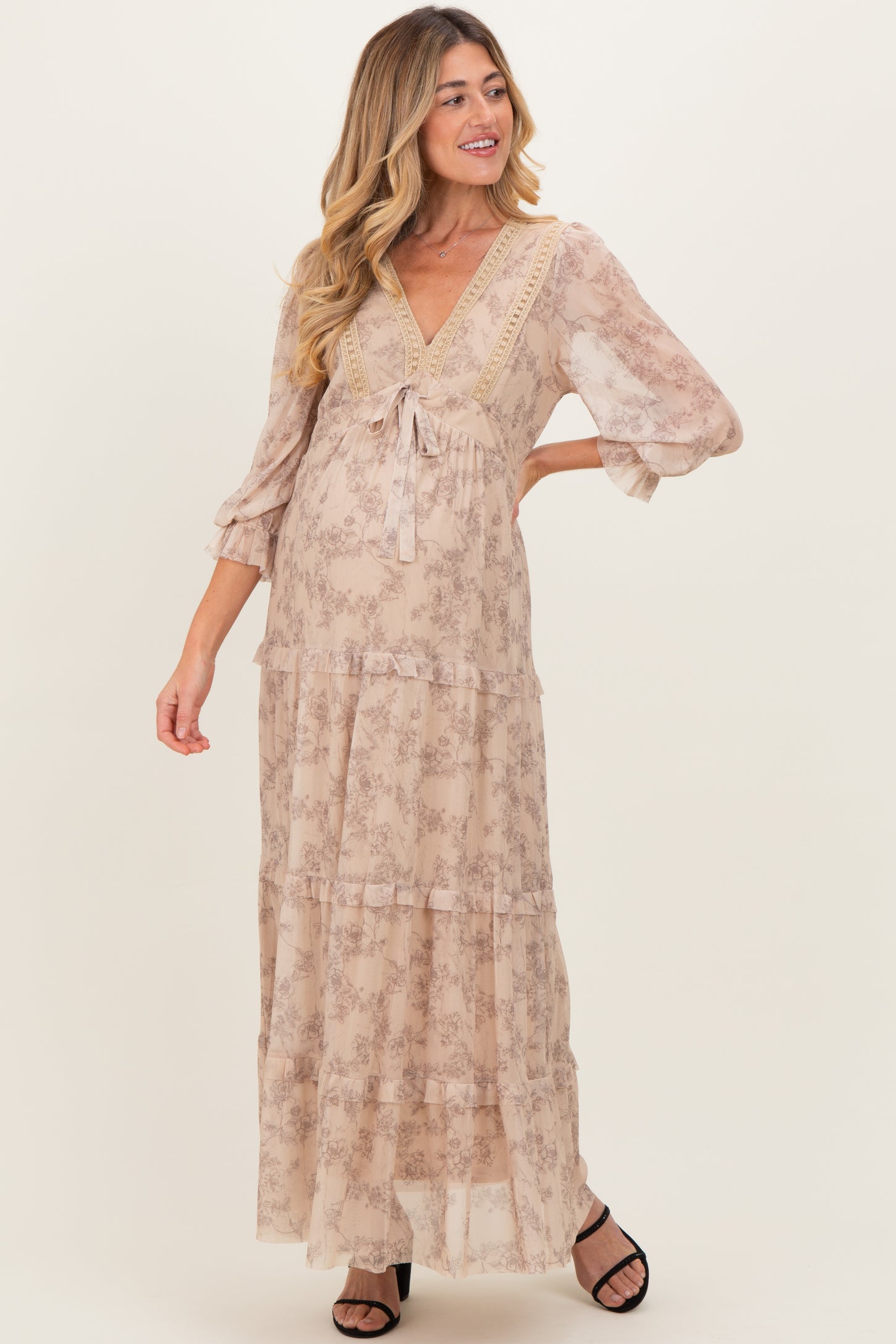 woman wearing a light floral print maternity maxi dress with a v-neckline and tiered ruffles, showing off her baby bump