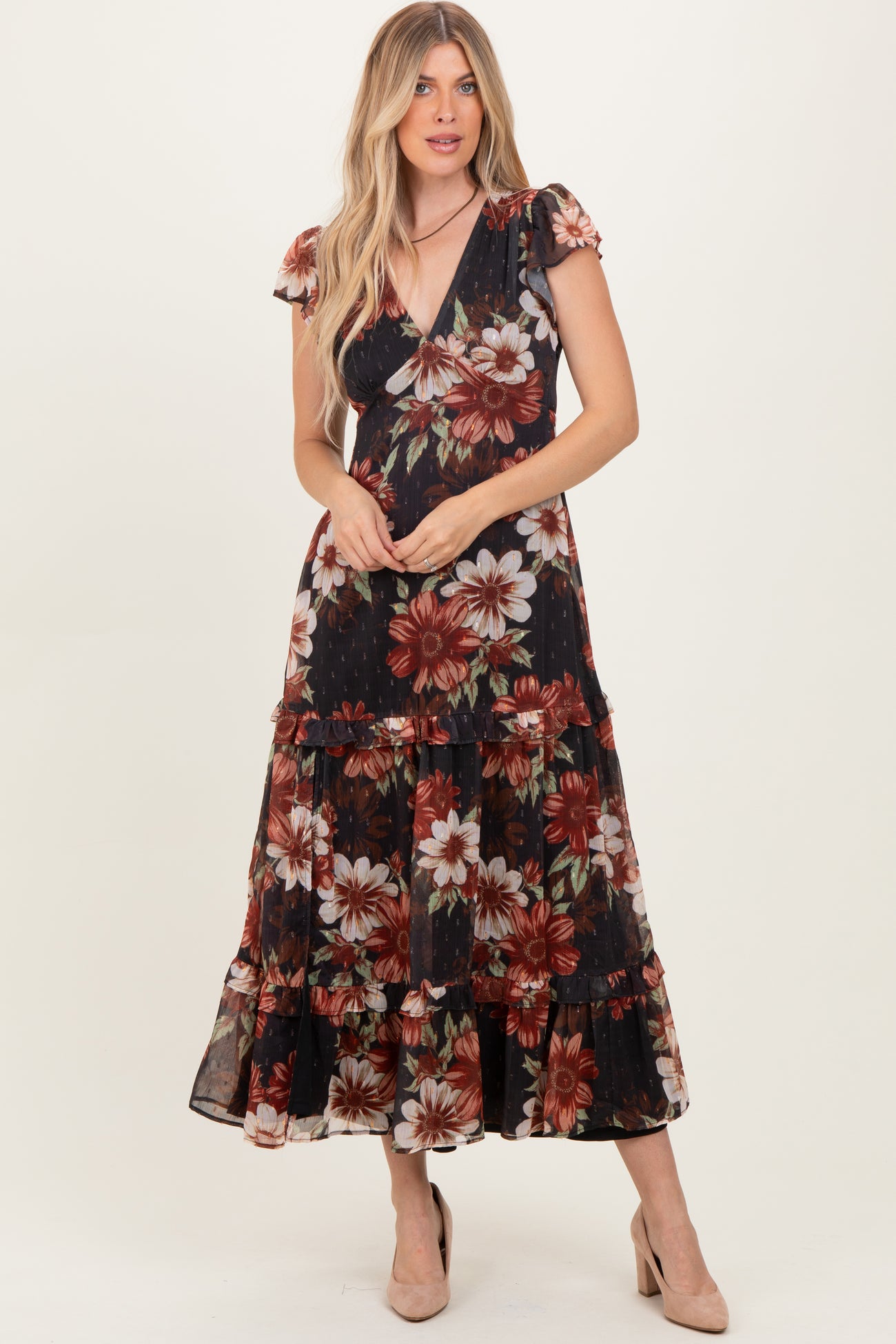 woman wearing a black floral maxi dress with short ruffle sleeves and tiered skirt, paired with nude heels