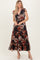 woman wearing a black floral maxi dress with short ruffle sleeves and tiered skirt, paired with nude heels