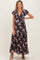 woman wearing a floral maxi maternity dress with short ruffled sleeves and a deep v-neck, posing with one hand on hip