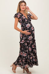 woman wearing a black floral maternity maxi dress, showing baby bump and standing with one hand on her belly