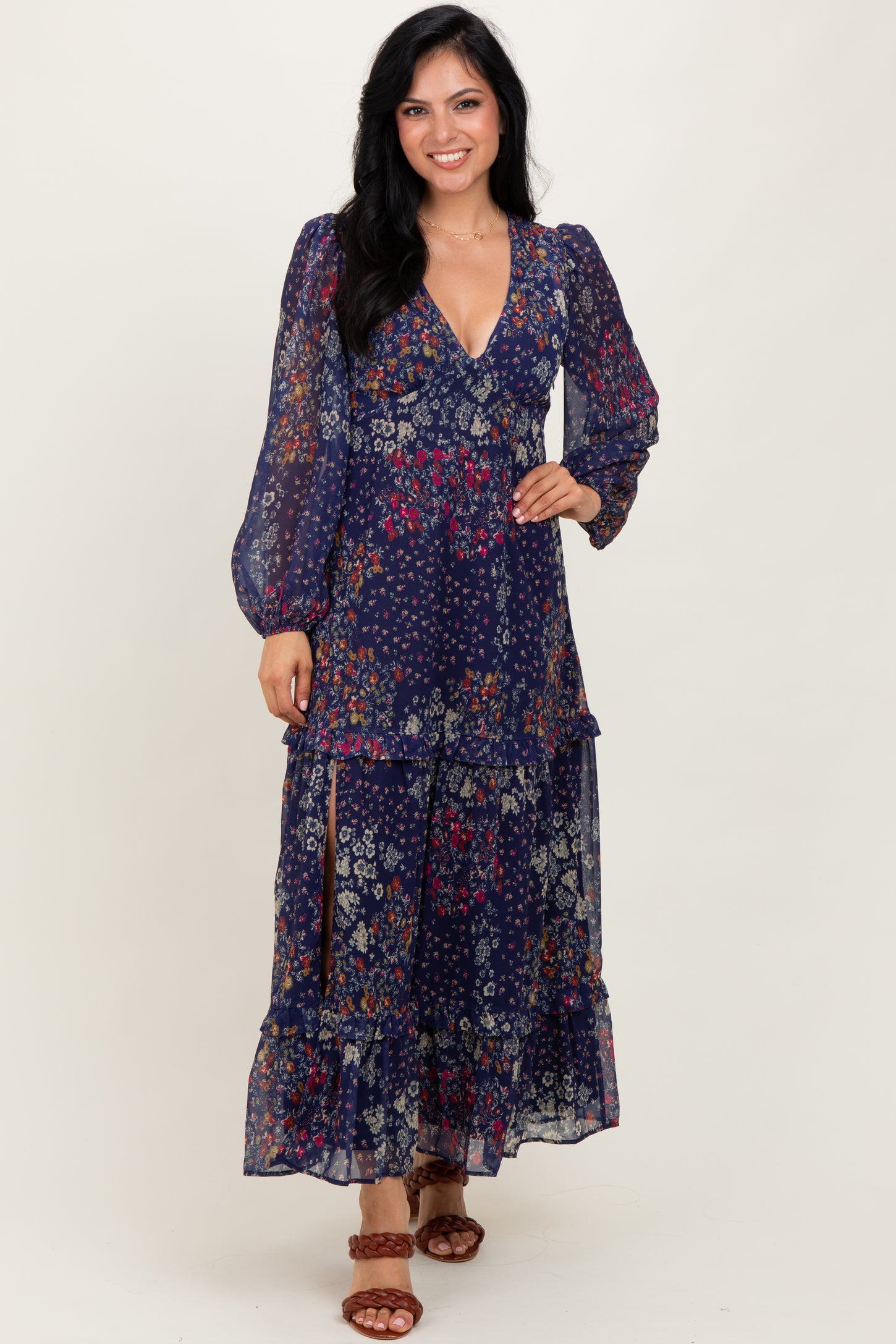 woman wearing a navy floral maxi dress with long sleeves and a tiered skirt, standing and smiling