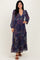 woman wearing a navy floral maxi dress with long sleeves and a tiered skirt, standing and smiling