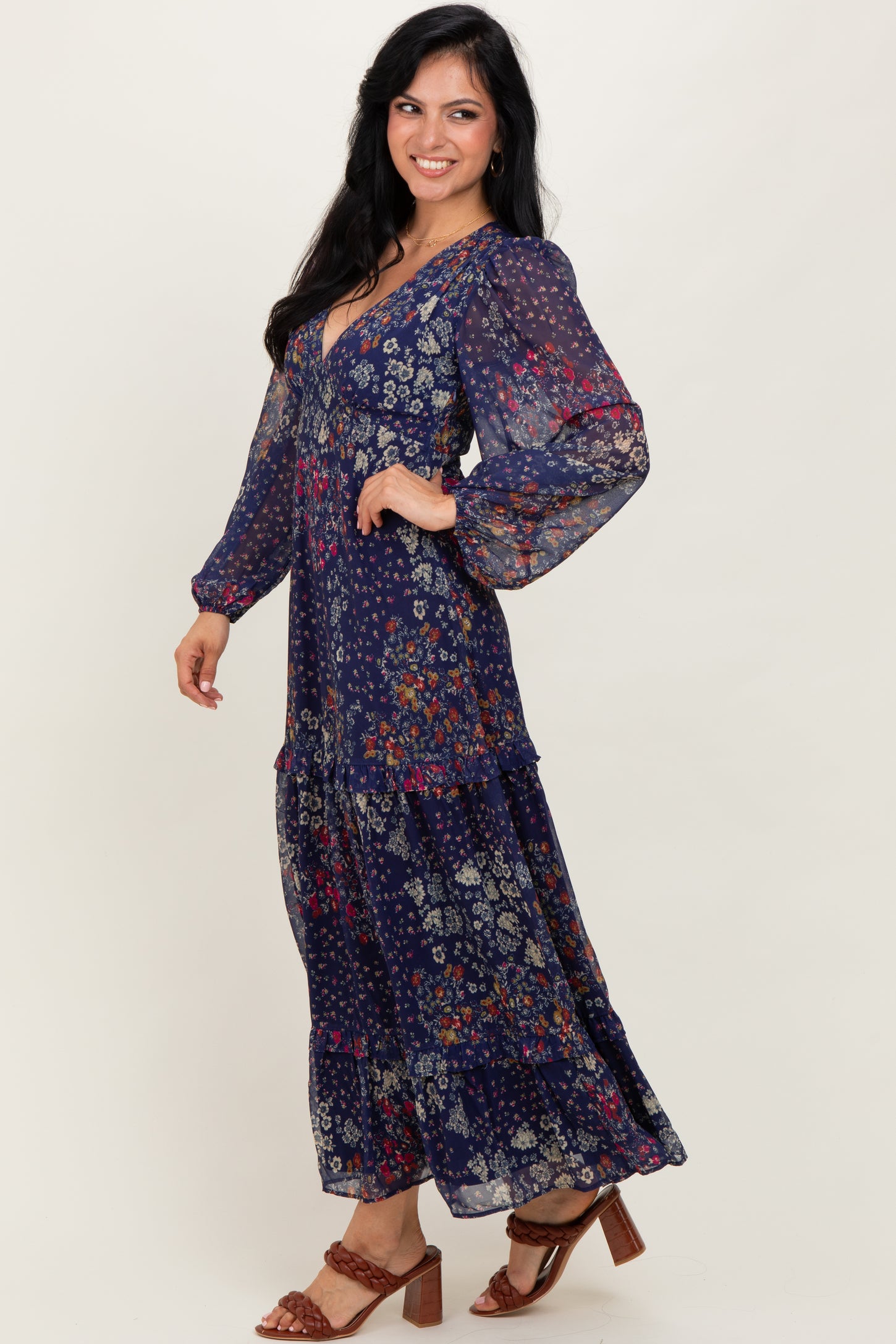 woman wearing a navy blue floral maxi dress with long sleeves and a tiered skirt, standing sideways