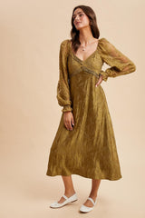 woman wearing an olive green long sleeve midi dress with puff sleeves and intricate detail on the bodice