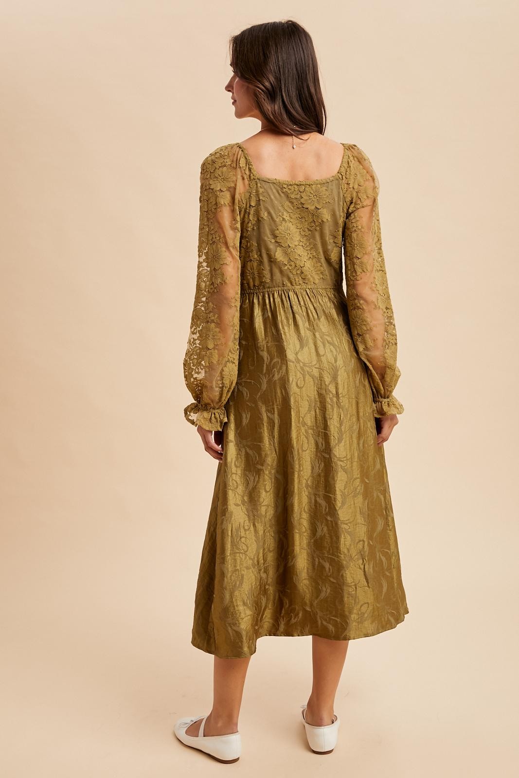 woman wearing a long olive green dress with sheer puff sleeves and floral details, viewed from the back