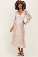 woman wearing a light beige maternity dress with lace long sleeves and a flowy skirt, showcasing her baby bump