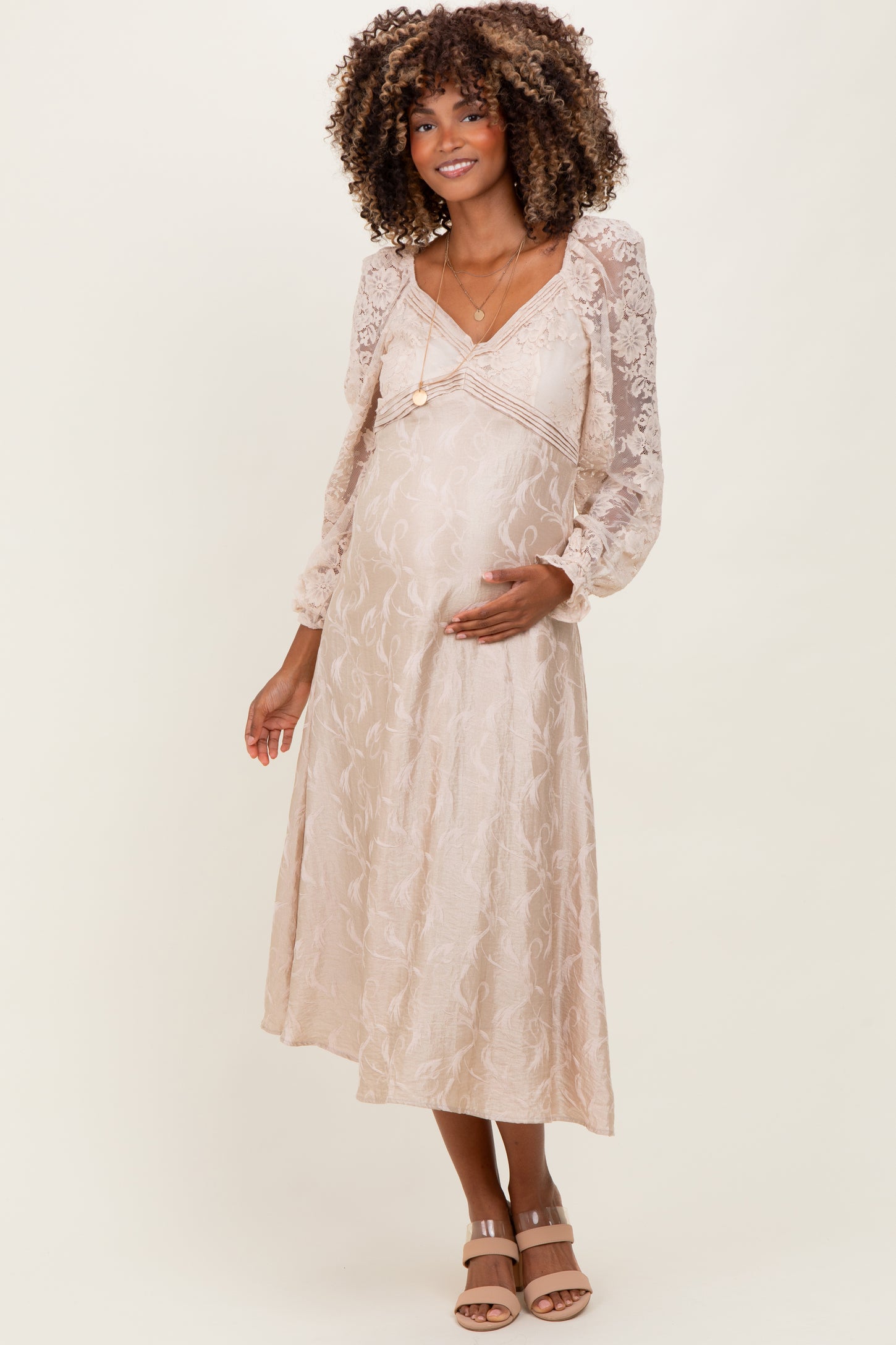 woman wearing a beige floral lace maternity dress with long puff sleeves and a baby bump visible
