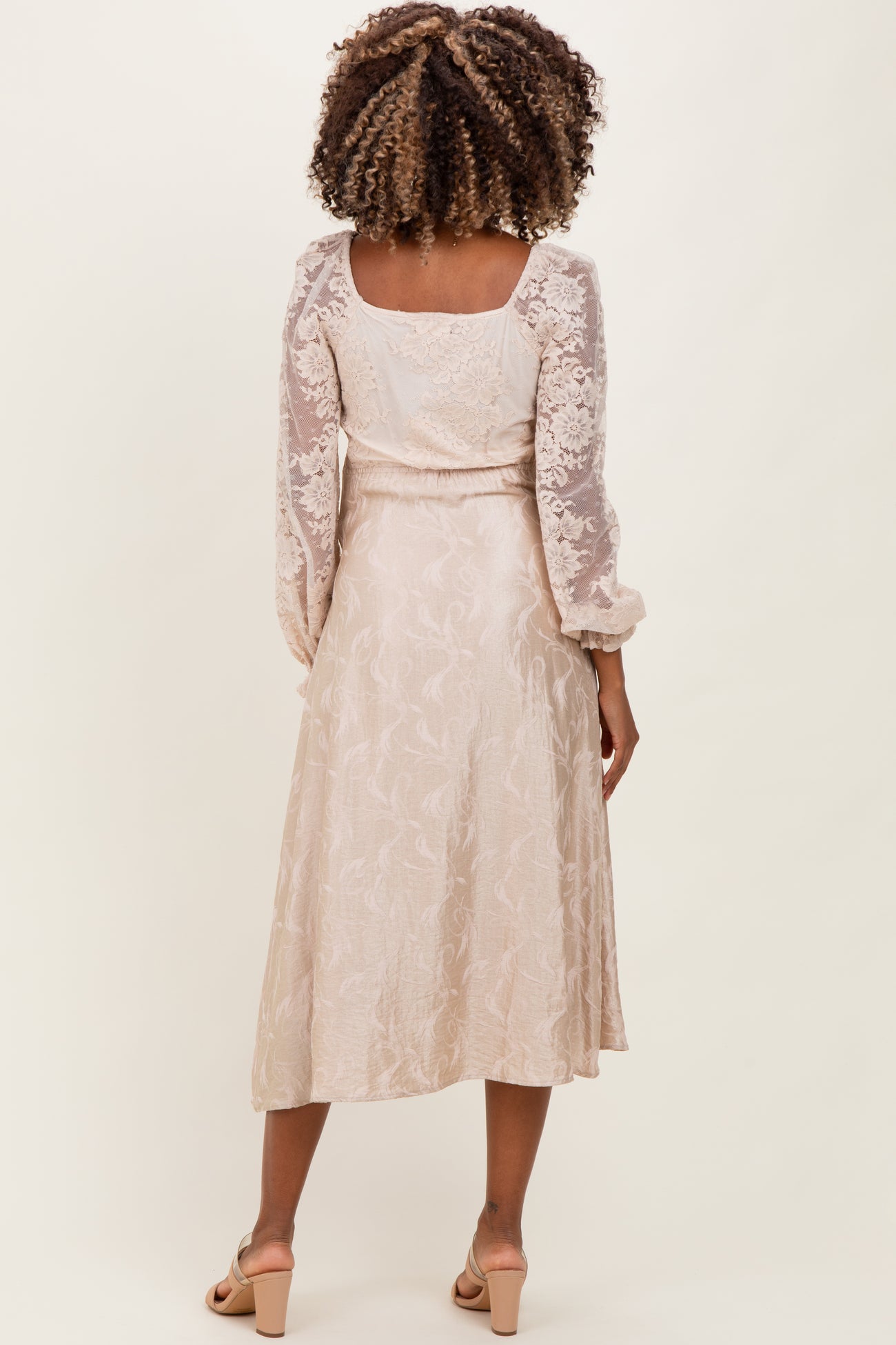 woman wearing a light beige maternity dress with sheer long sleeves and a flowy skirt, showing the back view