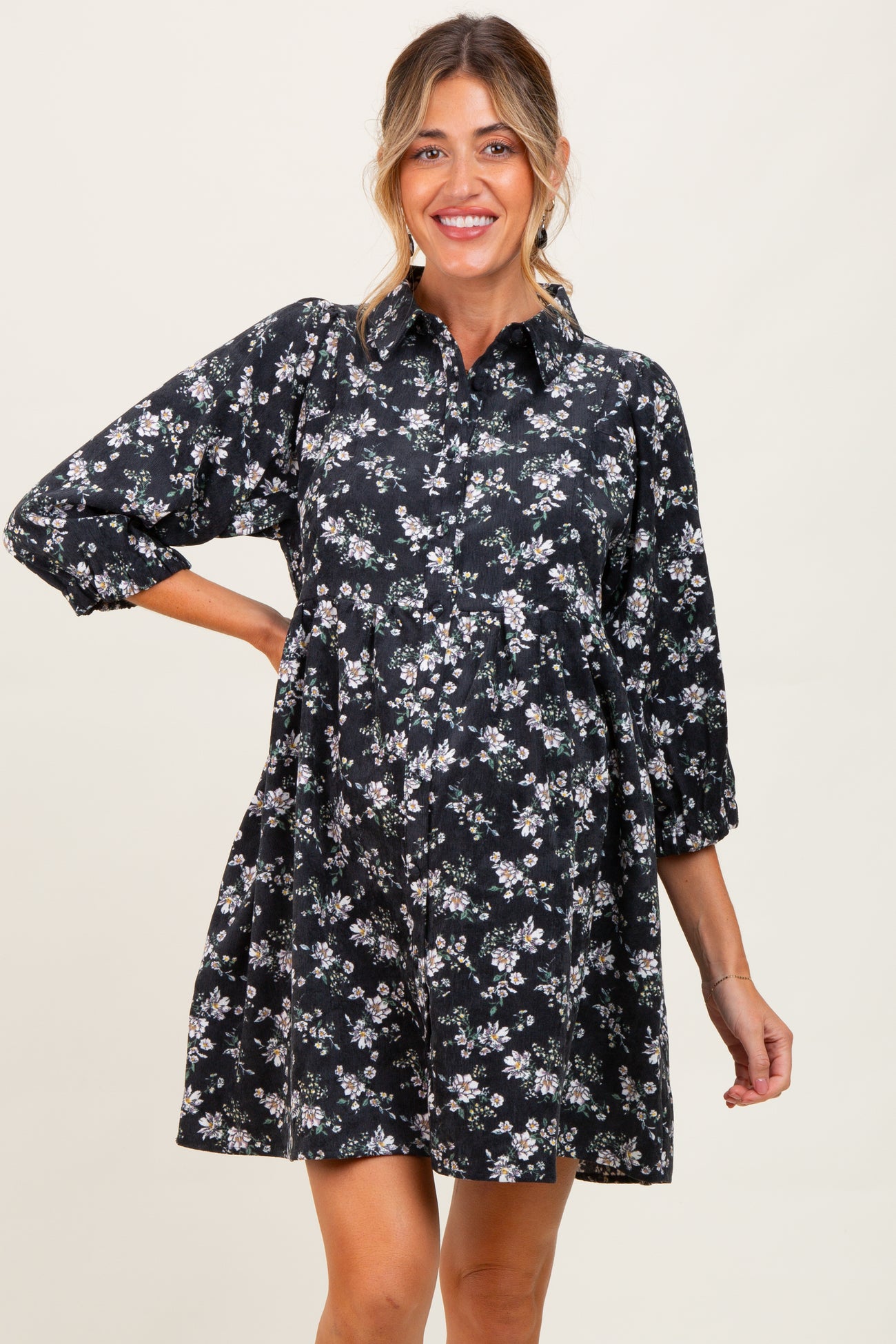 woman wearing a black floral maternity dress with a collared neckline and three-quarter sleeves, smiling and showcasing her baby bump