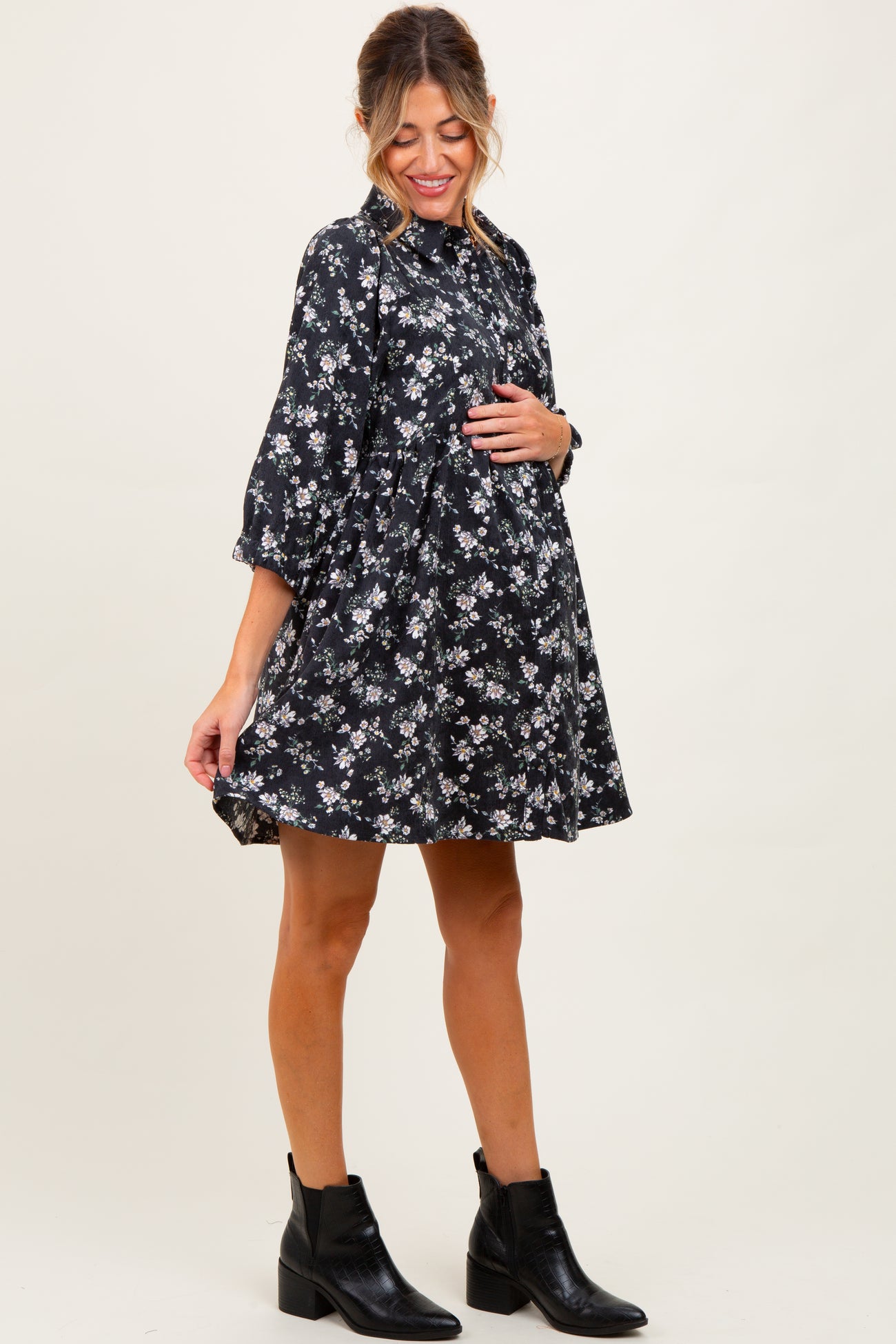 woman wearing a black floral maternity dress with a tiered silhouette and holding her baby bump