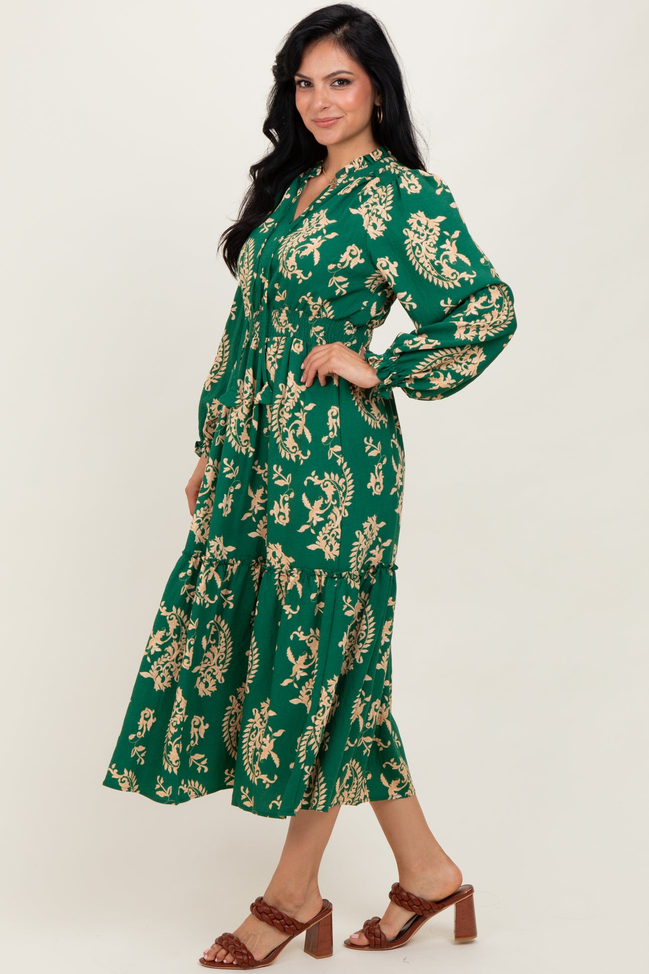 woman wearing a green floral print midi dress with long sleeves and a tiered skirt, standing profile on a light background