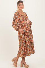 woman wearing a floral maternity maxi dress with long sleeves and pockets, gently cradling her baby bump