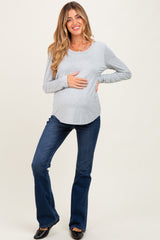 woman wearing a gray long sleeve maternity top and flared jeans, holding her baby bump
