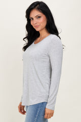 woman wearing a light grey long sleeve top with a scoop neckline, styled with blue jeans, standing against a neutral backdrop