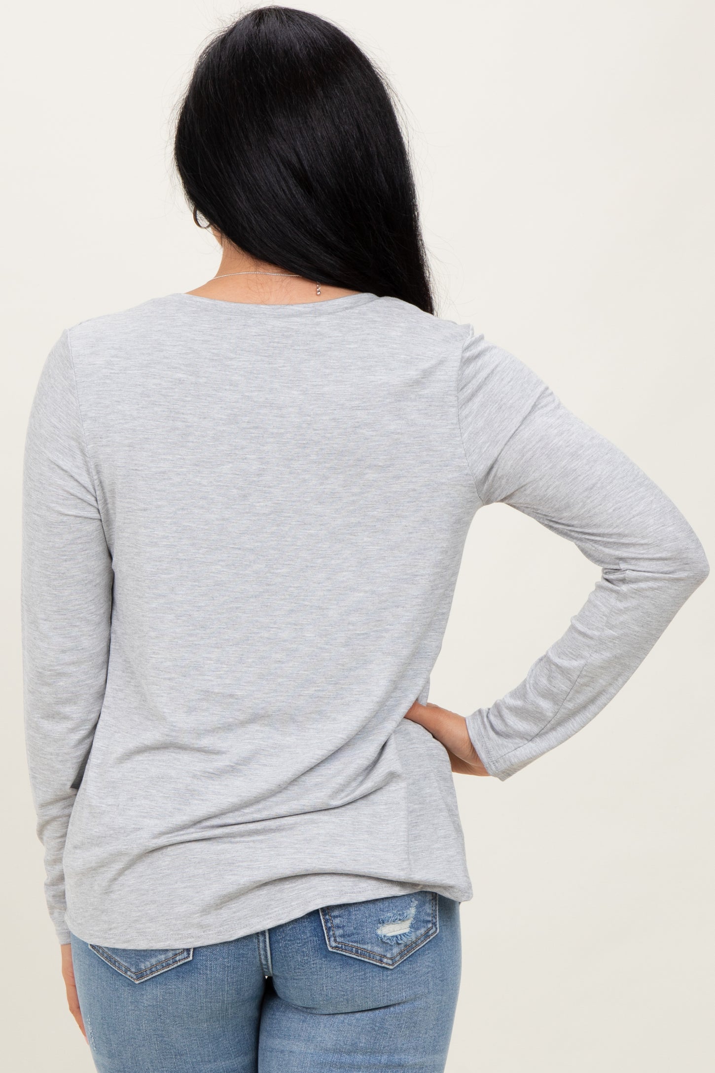 woman wearing a light gray long sleeve top, viewed from the back, paired with blue jeans