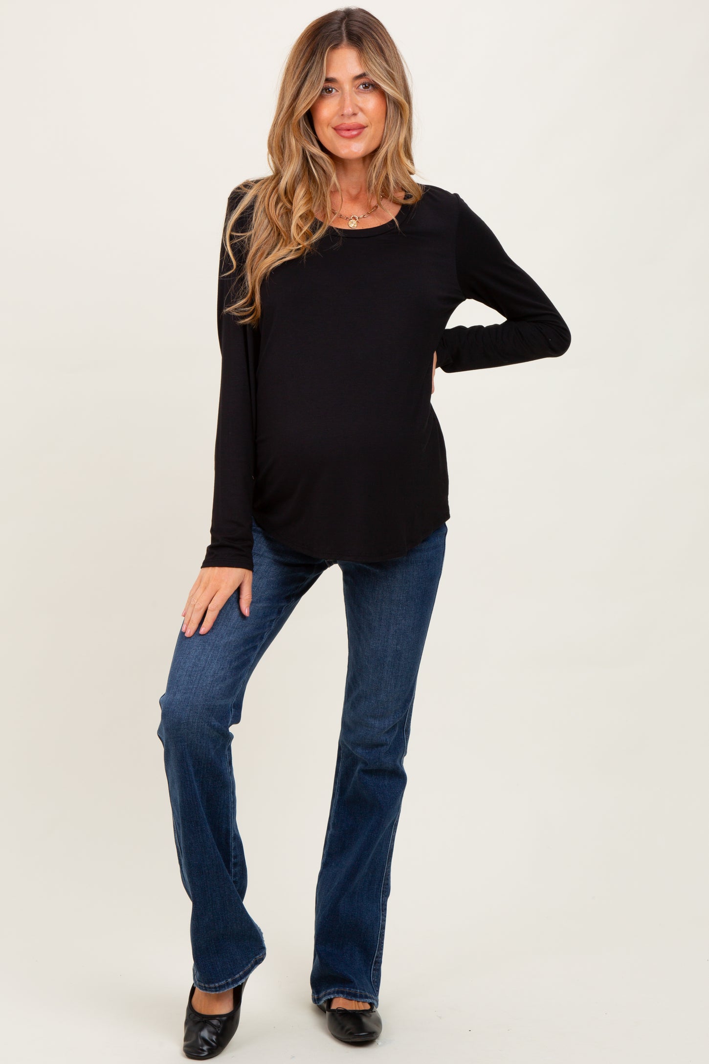 woman wearing a black long sleeve maternity top and blue flared jeans with a visible baby bump