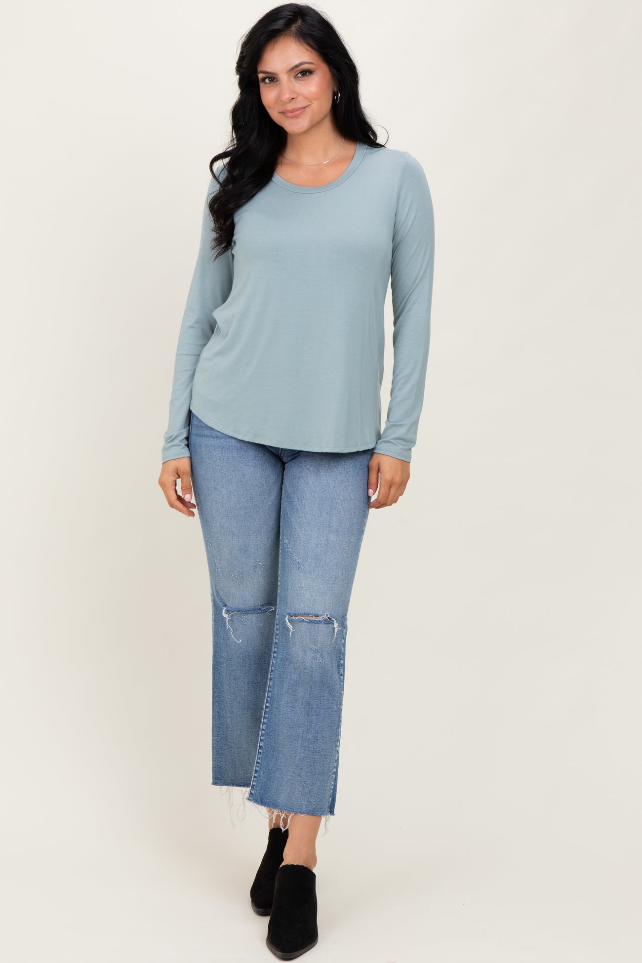 woman wearing a light teal long sleeve top and distressed light wash flared jeans with black ankle boots
