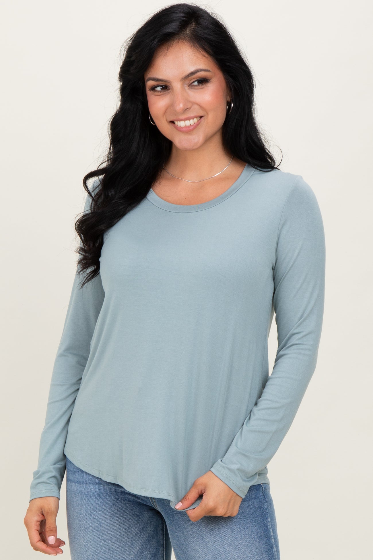 woman wearing a light blue long sleeve top with a rounded neckline and casual fit, standing and smiling