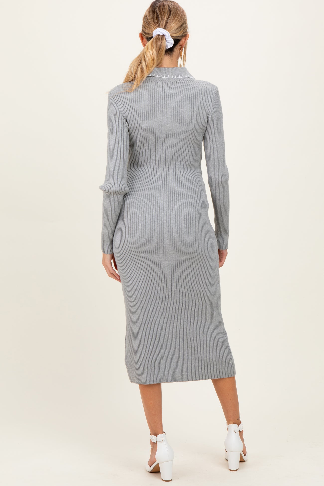 woman wearing a light grey ribbed maternity dress, view from the back, with a fitted silhouette and mid-calf length