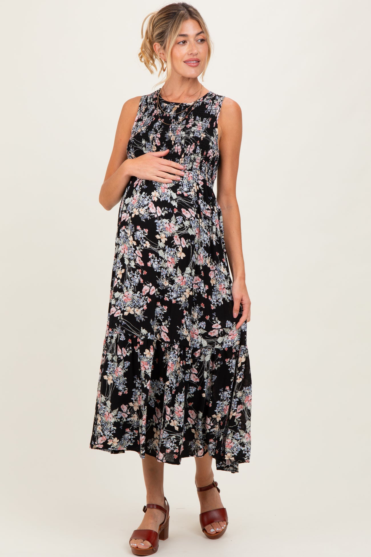 woman wearing a floral black maternity dress with a tiered skirt and holding her baby bump