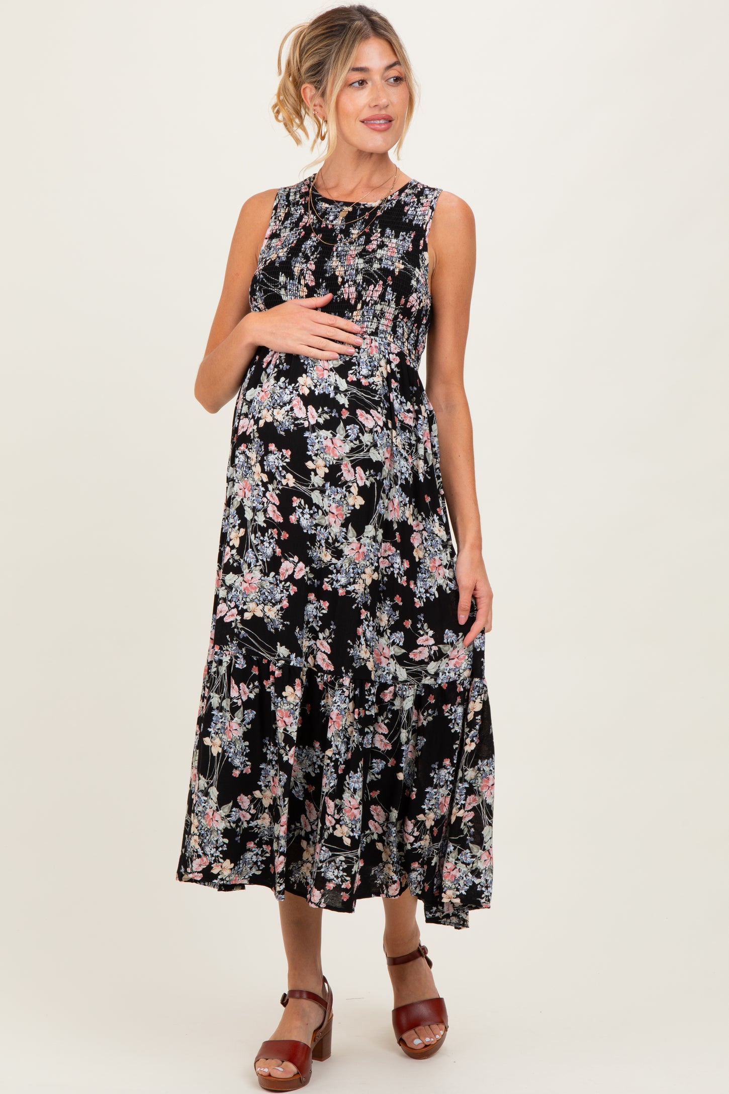 woman wearing a floral black maternity dress with a tiered skirt and holding her baby bump
