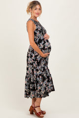 woman wearing a black floral maternity maxi dress with a tiered skirt and cradling her baby bump