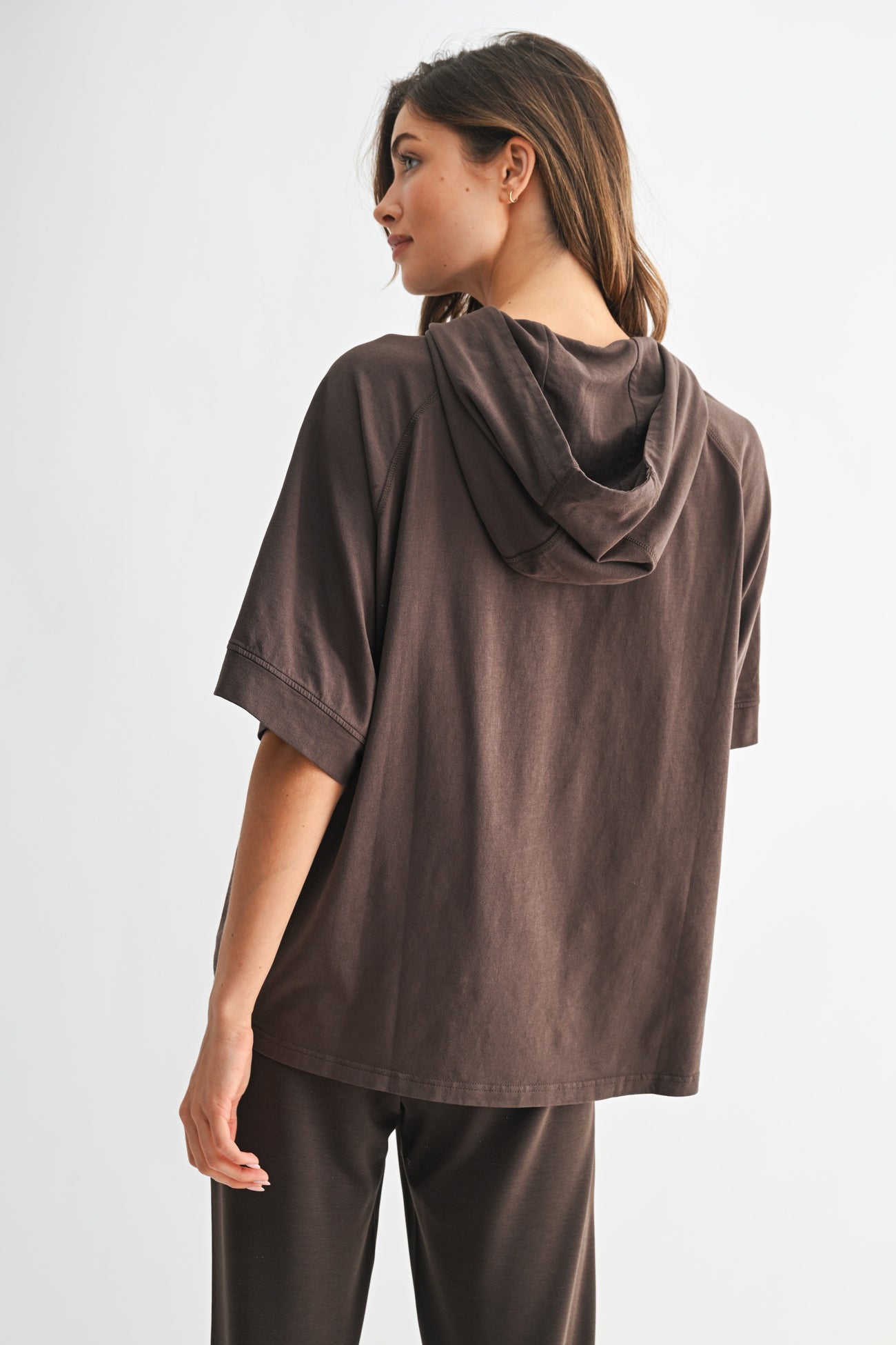 woman wearing a dark brown oversized hoodie with a hood and short sleeves, viewed from the back