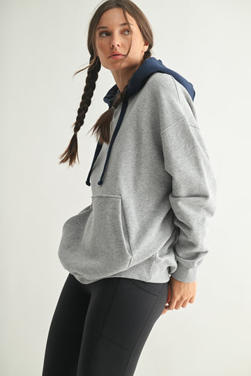 woman wearing a gray oversized hoodie with a navy blue hood and black leggings, posing with a braid in her hair