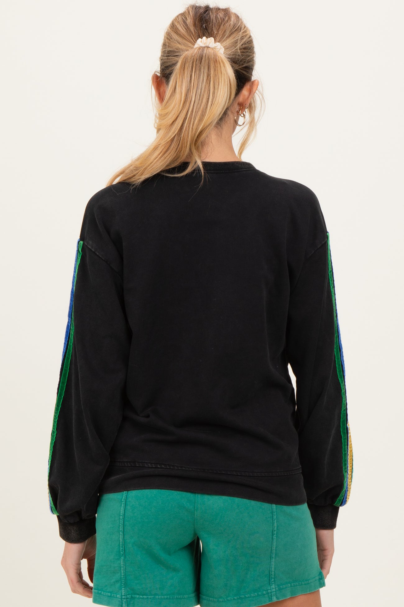 woman wearing a black maternity sweatshirt with colorful striped sleeves and styled with green shorts