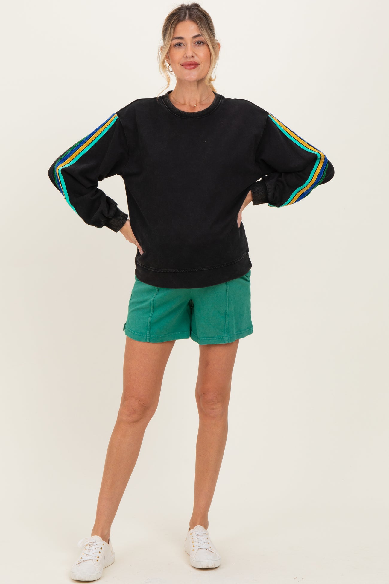 woman wearing a black maternity sweatshirt with colorful stripes on the sleeves and green maternity shorts