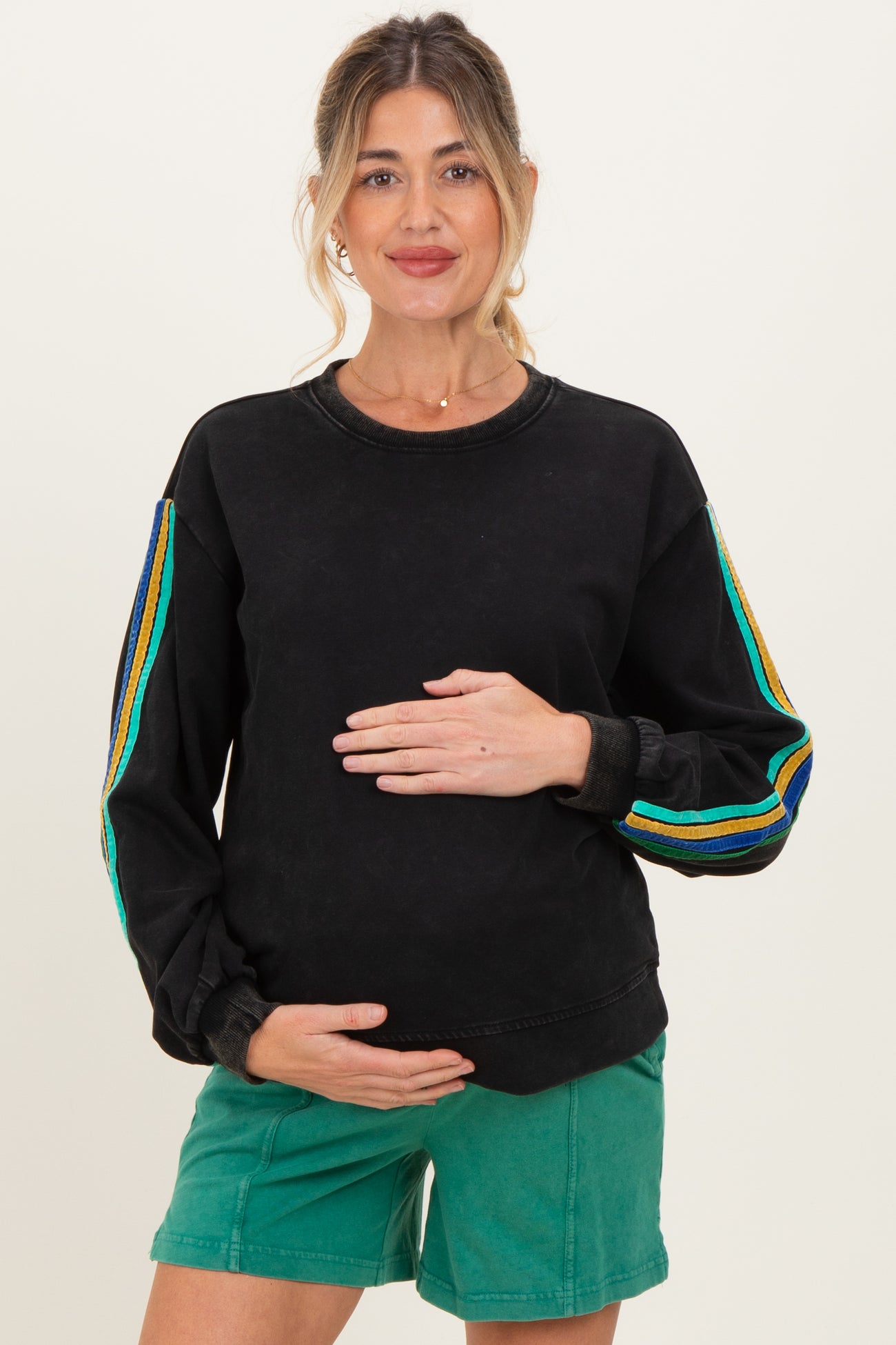woman wearing a black maternity sweatshirt with colorful stripes on the sleeves and holding her baby bump