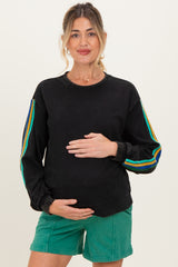 woman wearing a black maternity sweatshirt with colorful stripes on the sleeves and holding her baby bump