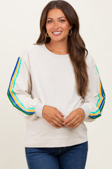 woman wearing a cream maternity sweatshirt with colorful striped sleeves and a relaxed fit, smiling at the camera