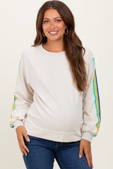 woman wearing a light beige maternity sweatshirt with colorful striped details on the sleeves and a visible baby bump