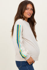 woman wearing a cream maternity sweatshirt with colorful stripes on the sleeves and a visible baby bump