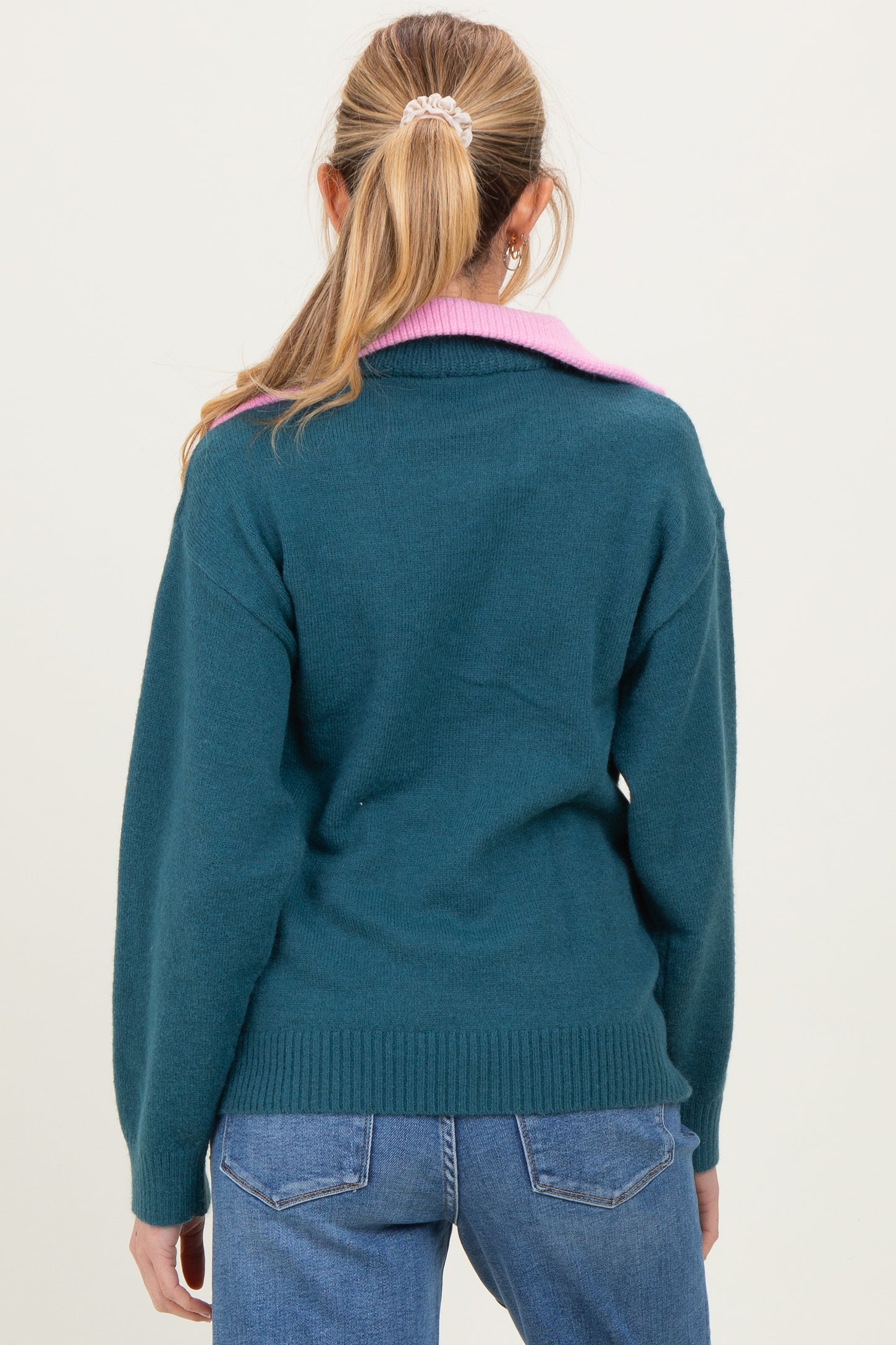 woman wearing a teal maternity sweater with a pink collar, seen from the back, paired with blue jeans