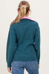 woman wearing a teal maternity sweater with a pink collar, seen from the back, paired with blue jeans