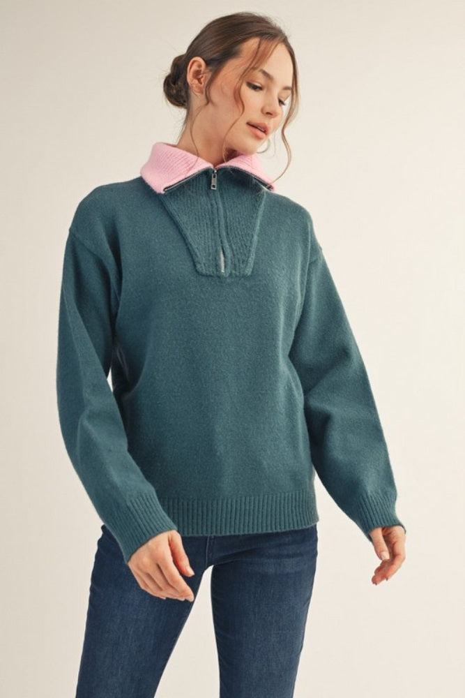 woman wearing a dark teal half-zip sweater with a pink collar and casual jeans