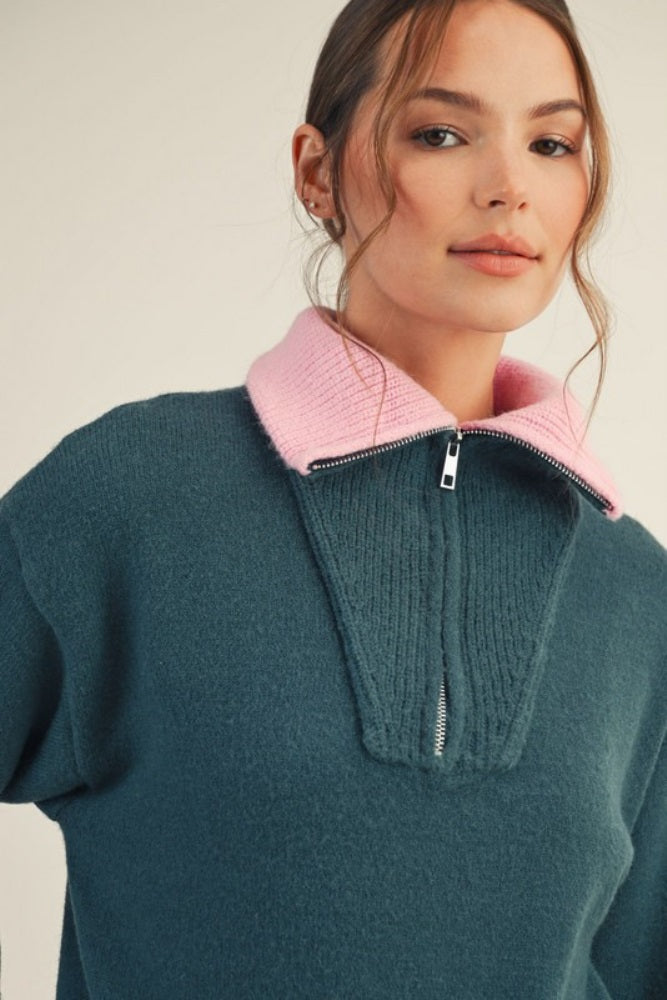 woman wearing a teal pullover sweater with a pink collar and half zipper detail