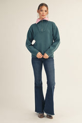 woman wearing a dark teal quarter-zip pullover sweater with a pink collar and flared jeans