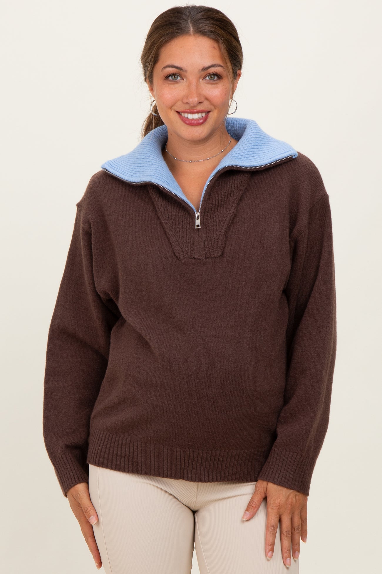 woman wearing a brown maternity pullover sweater with a light blue collar and zipper detail