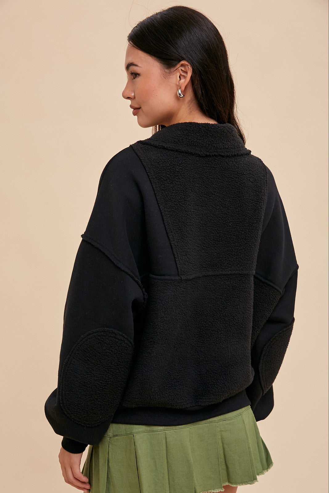 woman wearing a black oversized sweatshirt with fleece panels and a green pleated skirt