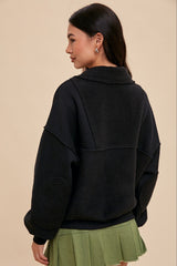 woman wearing a black oversized sweatshirt with fleece panels and a green pleated skirt