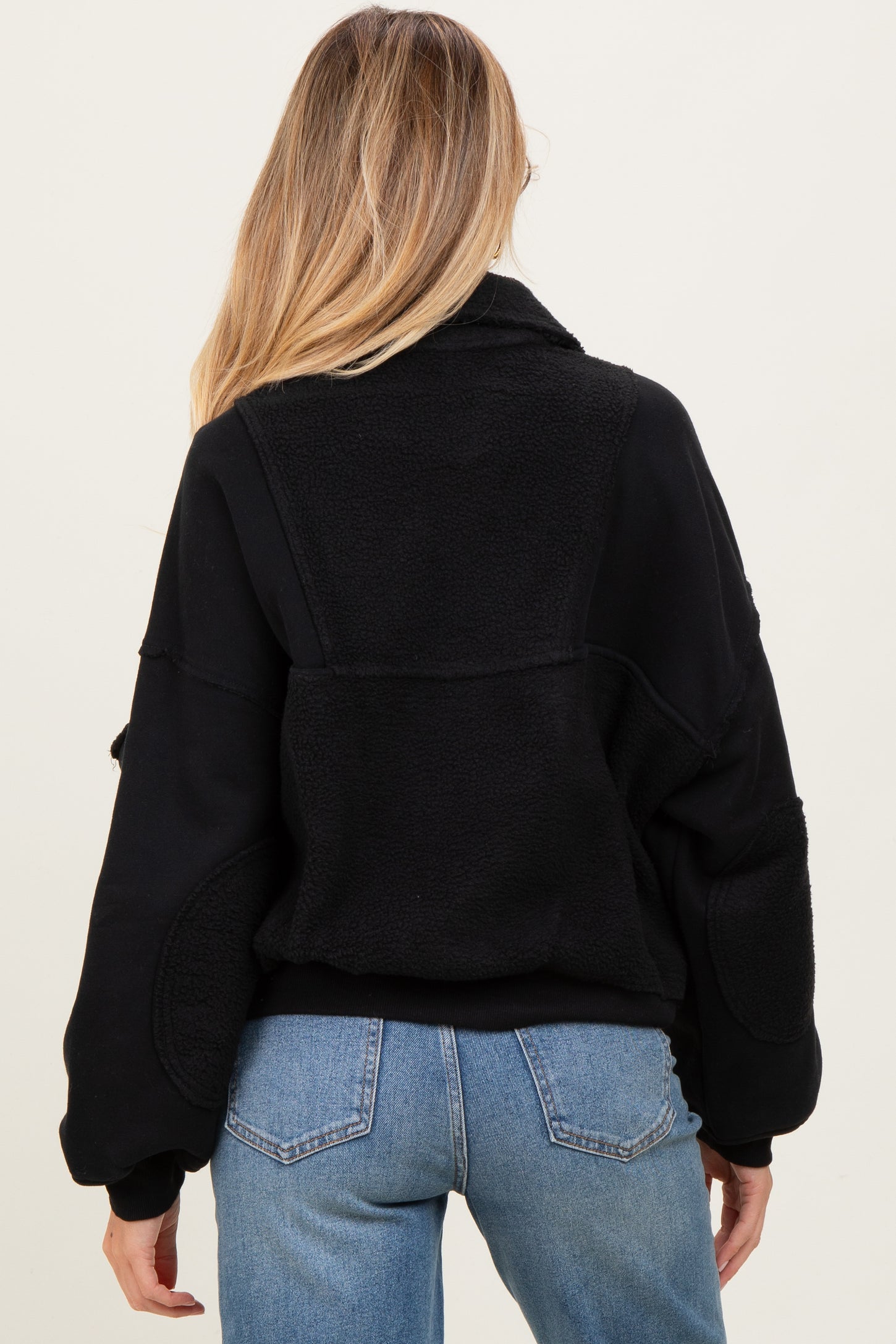 woman wearing a black maternity fleece jacket with a relaxed fit, showing the back view and paired with light blue jeans