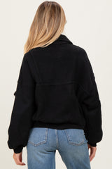 woman wearing a black maternity fleece jacket with a relaxed fit, showing the back view and paired with light blue jeans